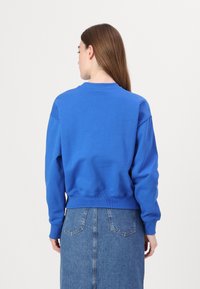 Felpa blu in cotone con maniche lunghe, polsini a coste e scollatura a girocollo. Abbinata a una gonna in denim con tasche posteriori e una forma aderente.