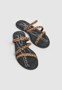 Sandales plates avec trois brides imprimées léopard sur une semelle noire présentant une texture lisse et un détail logo signature.