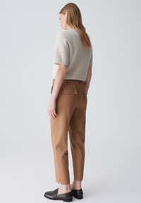 Beige gestrickter Pullover, braune schmal geschnittene Hose mit Taschen und schwarze Slipper. Das Outfit zeichnet sich durch eine lockere Passform und weiche Texturen aus.