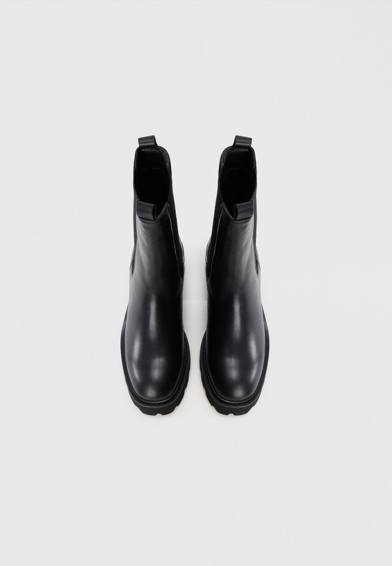 Par de botas Chelsea de cuero negro con suelas gruesas, lengüetas en el tobillo y paneles laterales elásticos sobre un fondo blanco.