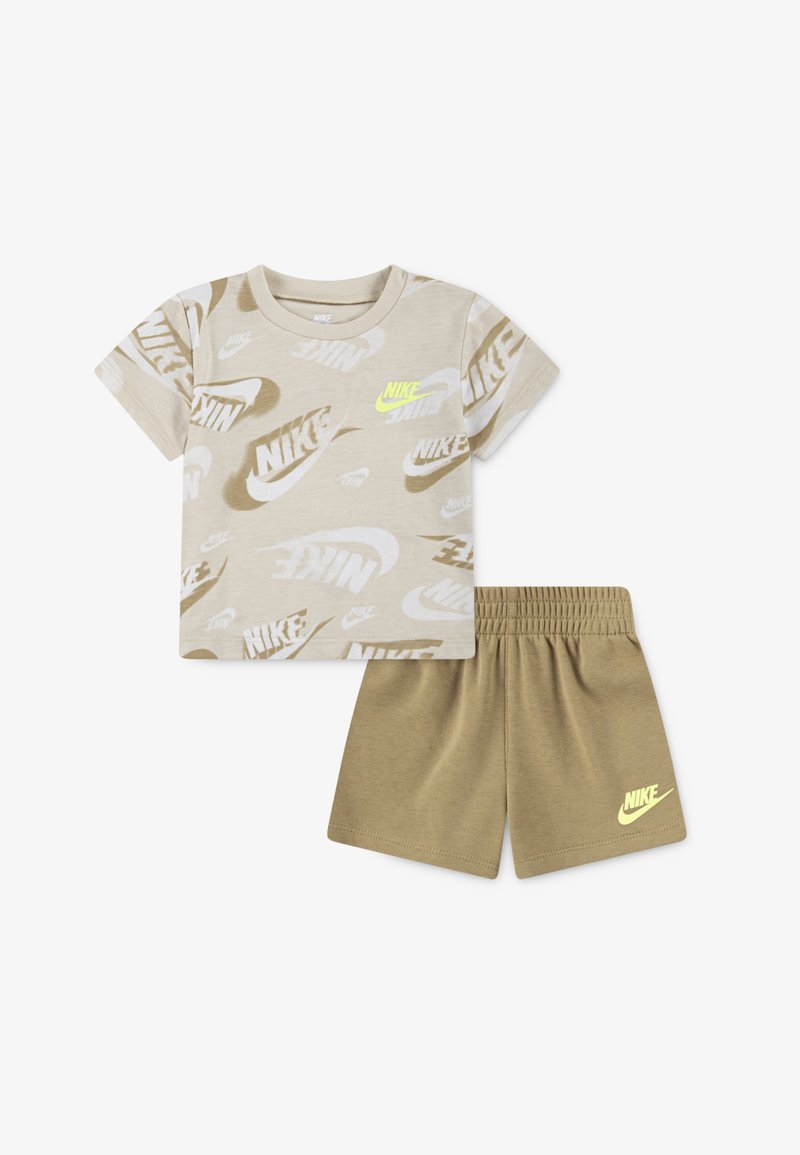 Bež majica s kratkimi rokavi z večkratnimi logotipi Nike v različnih odtenkih in neon rumenim logotipom. Ujemajoče bež kratke hlače z elastičnim pasom.