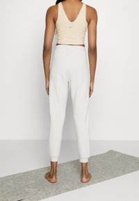 Top sportivo beige con schiena a V e logo discreto, abbinato a pantaloni della tuta grigi chiari con polsini a costine e logo abbinato nella vita.