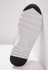 Suela de zapato Nike, que presenta un talón de goma negra texturizada, una entresuela blanca con un patrón de banda de rodadura geométrico y un logotipo de la marca distintivo grabado.