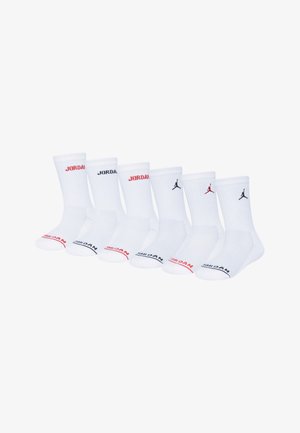 Meias atléticas brancas com textura canelada, com a marca 'JORDAN' em vermelho e preto, e o logótipo Jumpman em preto. Seis pares expostos.