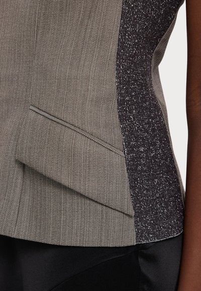 Aansluitend mouwloos vest in grijze textuurstof met een donker, glanzend zijpaneel en geplooide details nabij de taille.