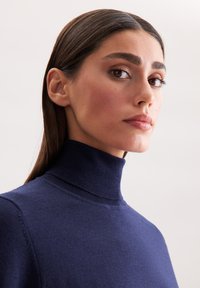 Granatowy sweter z golfem o dopasowanym kołnierzu, gładkiej teksturze i ribbowanych detalach. Projekt jest prosty i elegancki, z minimalną liczbą szwów.