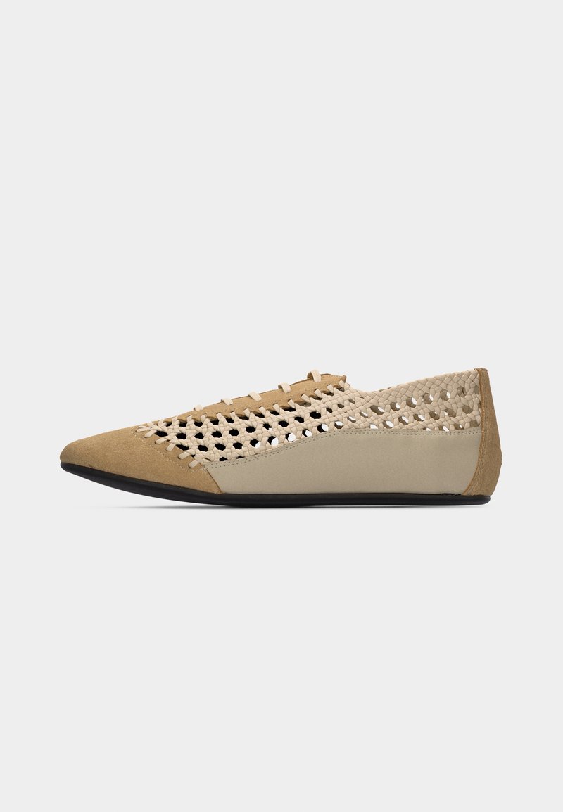 Chaussure plate beige à bout pointu avec un design supérieur tissé, comprenant des panneaux en cuir lisse et en daim, et une semelle noire.