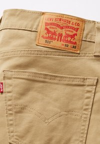 Kaki denimbyxor med en framträdande läderetikett med röd tryck. Klassisk Levi's-logotyp och sömnad på bakfickan. Storlek W32 L32.