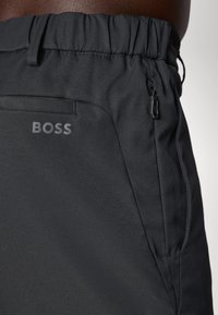 Juodi sportiniai šortai su elastingu juosmeniu, šonine užtrauktuko kišene ir subtiliu "BOSS" logotipu, esančiu apatiniame priekio kampe. Lygi tekstūra.