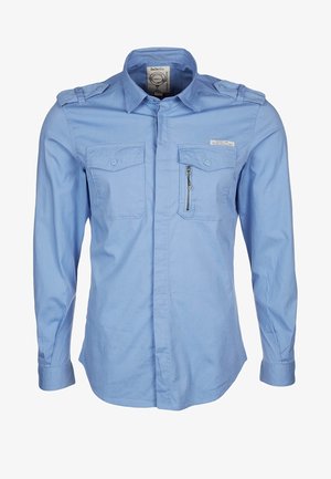 Jasnoniebieska koszula z długim rękawem z dwiema kieszeniami na piersi, z zapięciami na guziki oraz kieszenią na zamek. Posiada naramienniki i gładką teksturę.