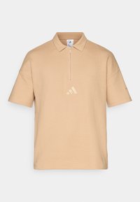 Beige polo shirt met een kwart ritssluiting, gestructureerde stof en korte mouwen. Voorzien van een subtiele gouden Adidas-logo op de borst.