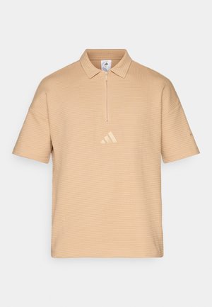 Camisa polo beige com fecho de ¼, tecido texturizado e mangas curtas. Apresenta um discreto logo dourado da Adidas no peito.
