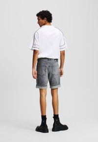 Camisa blanca de manga corta con detalles en negro, combinada con pantalones cortos de mezclilla gris. El modelo lleva botas negras hasta el tobillo y calcetines negros.
