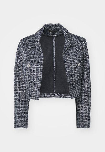 Gekürzte Jacke aus navy- und weißen Tweed mit langen Ärmeln, Reverskragen und geknöpften Brusttaschen, vor einem schlichten Hintergrund präsentiert.