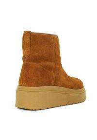 Bruine suede enkellaarsjes met een ronde neus, voorzien van een dikke tan platformzool en een trekclip aan de achterkant voor eenvoudig aan- en uittrekken.