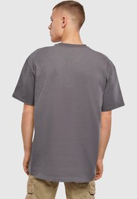 Graues Kurzarm-T-Shirt mit lockerer Passform, Rundhalsausschnitt und glatter Textur, von hinten betrachtet mit sichtbaren Nähten und Konturen.