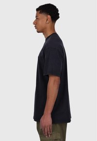 Schwarzes Baumwoll-T-Shirt mit kurzen Ärmeln und Rundhalsausschnitt, das eine lockere Passform aufweist. Sichtbare Nahtdetails am Saum und an den Ärmeln.