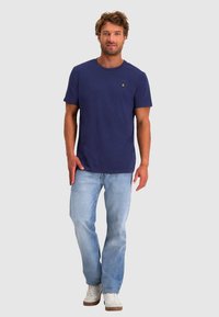 Navyblauwe katoenen t-shirt met een ronde hals, gecombineerd met lichtblauwe denim jeans. Witte sneakers maken de casual outfit compleet.