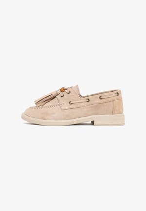 Beige suède loafer met kwastjes, decoratieve veters aan de zijkanten, lage blokhak en ronde houten kraal bovenop.