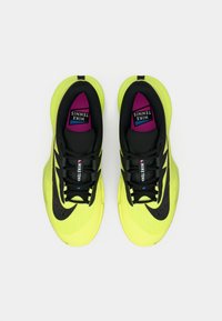 Λαμπερά κίτρινα αθλητικά παπούτσια τένις με μαύρες λεπτομέρειες, χαρακτηριστικά υφαντής σχεδίασης, επενδεδυμένο λαιμό και πολύχρωμο λογότυπο στις σόλες.