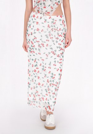 Witte maxi rok met een bloemenpatroon van kersen in roze en groen. Gemaakt van lichtgewicht, doorzichtig materiaal; gecombineerd met grijze en beige sneakers.