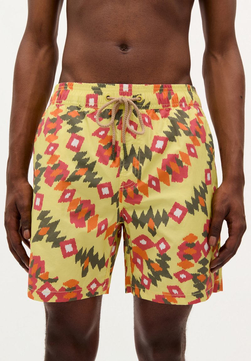 Shorts de bain jaune vif avec un motif géométrique en rouge, rose, vert et noir. Comprend une taille élastique avec un cordon de serrage.