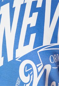 Modrá látka s velkým bílým potiskem textu a částečným zdobeným číslem "9" a emblémem štítu se slovem "ORIGINAL."