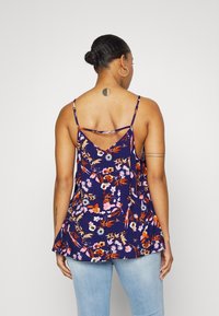 Kukka-tankkitoppi tummansinisen taustan kanssa, jossa on ohuet olkaimet, V-muotoinen selkäosa ja monivärisiä kukkia vaaleanoransseissa, liiloissa ja sinisissä sävyissä.