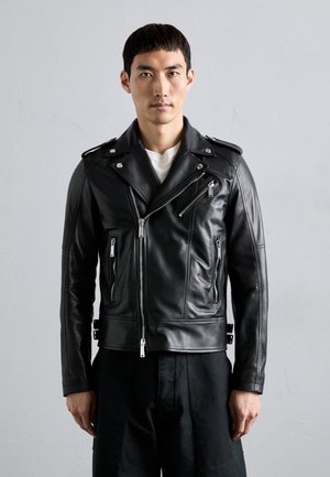 Chaqueta de motorista de piel negra con cremalleras y herrajes plateados, que presenta una cremallera frontal en ángulo, bolsillos laterales y un diseño ajustado.