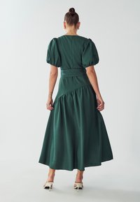 Vihreä, polvimittainen mekko, jossa on puffihihat, tiukka vartalo ja kootut vyötärölinjat. Suuri tekstuuri ja minimalistinen muotoilu.