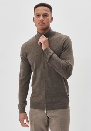 Brauner Reißverschluss-Pullover mit langen Ärmeln, hohem Kragen, gerippten Bündchen und glatter Textur, kombiniert mit hellen Hosen.