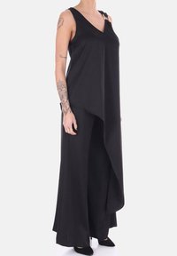 Abito lungo senza maniche di colore nero con orlo asimmetrico, texture liscia e dettaglio a spallina singola, dotato di pantaloni larghi e morbidi sotto.