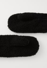 Pair of black fuzzy mittens made from soft, textured fabric, laid flat on a white surface.