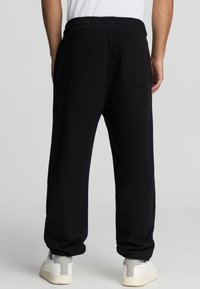 Pantaloni neri in felpa morbida, dotati di una vita elasticizzata e una singola tasca posteriore. Le gambe si restringono delicatamente verso i polsi.