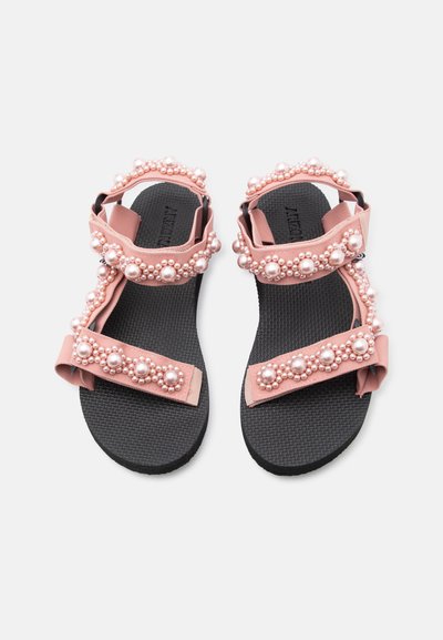 Μαύρα σανδάλια με σόλα, με ροζ υφασμάτινους ιμάντες στολισμένους με μεγάλα και μικρά ροζ μαργαριτάρια, στερεωμένα με κλεισίματα Velcro.