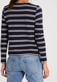 Top de rayas azul marino y blanco de manga larga combinado con jeans de mezclilla azul claro. El top presenta un escote redondo y textura acanalada.