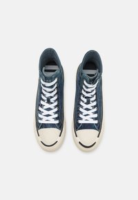 Tênis altos feitos de denim azul com cadarços brancos e uma sola de borracha creme. Apresenta um bico arredondado e um detalhe preto ao longo da sola.