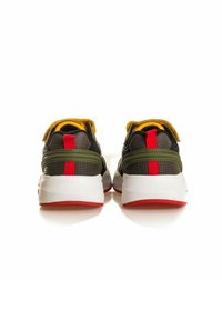 Zapatillas deportivas con una parte superior negra y detalles en verde, cuello amarillo, plantilla trasera roja y una entresuela blanca con una suela roja.