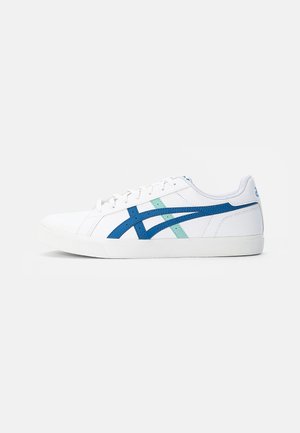 Witte lage sneaker met blauwe en lichtgroene streepaccenten en een witte rubberen zool op een effen lichtgrijze achtergrond.