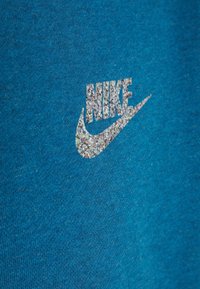 T-shirt in cotone blu con logo Nike glitterato argento sullo fronte. Il tessuto ha una superficie morbida e testurizzata.