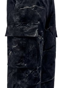 Sorte cargobukser med stor sidelomme og hvid marmoragtig tekstur på stoffet.