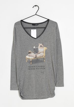 Chemise grise à manches longues avec un chat se prélassant sur une chaise dorée lisant un livre intitulé KATUSUTRA et texte "The more you read the more you know."