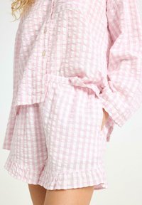 Ljust rosa rutigt loungewear-set gjort av textil med struktur; har knappar, en ficka och volangkanter på shortsen och ärmarna.
