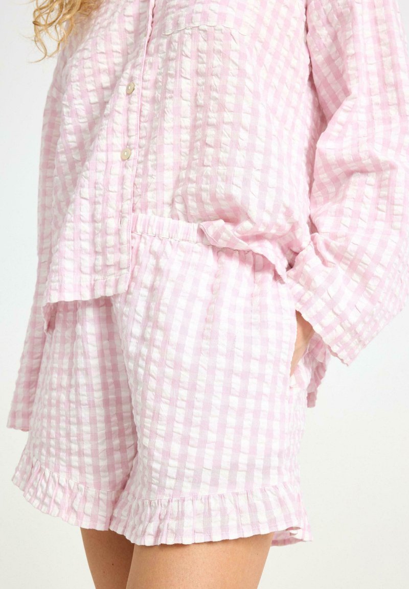 Ljust rosa rutigt loungewear-set gjort av textil med struktur; har knappar, en ficka och volangkanter på shortsen och ärmarna.
