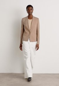 Beige tailored blazer with a single button closure, paired with a light shirt and white high-waisted trousers; smooth fabric, minimalistic design.