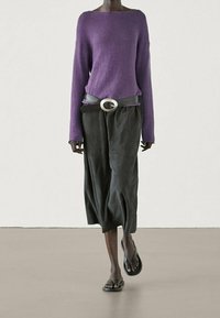 Pull tricot violet à large encolure, associé à un pantalon culotte gris foncé avec une ceinture à grosse boucle circulaire. Sandales noires complètent le look.
