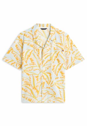 Camisa de manga corta con botones y estampado de hojas tropicales amarillas sobre fondo blanco, con un pequeño bolsillo en el pecho con el logo.