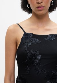 Μαύρο αμάνικο φόρεμα με περίπλοκα μαύρα λουλουδάτα κεντήματα και λεπτές τιράντες, με απαλό υφασμάτινο ματ. 