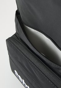 Sac en tissu noir avec une surface texturée, comportant un intérieur argenté et deux compartiments zippés pour un rangement sécurisé.