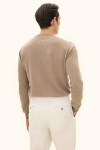 Hellbraun pullover aus einem weichen, strukturierten Stoff, mit langen Ärmeln und einem runden Ausschnitt, kombiniert mit weißen Cordhosen mit Gesäßtaschen.